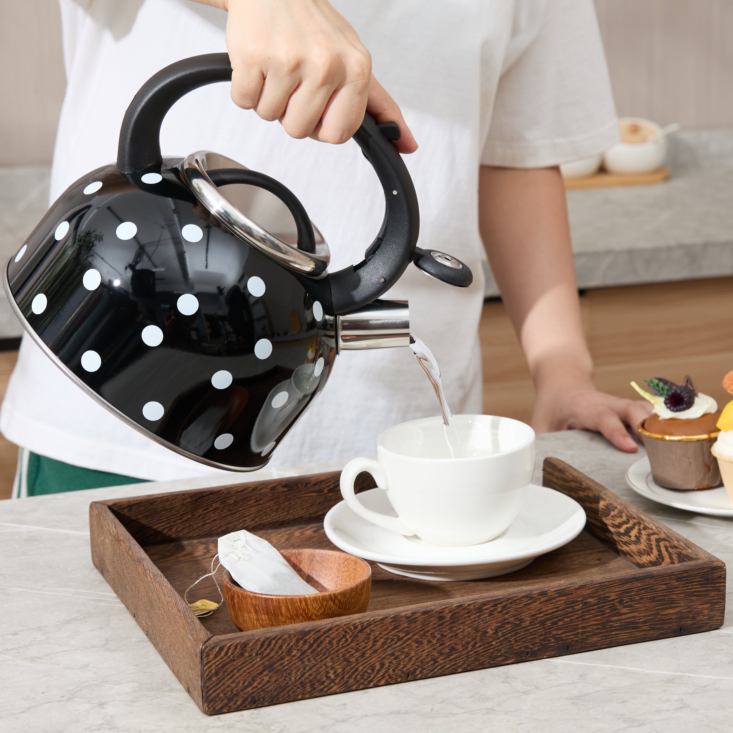 A real image of the black polka dot kettle showing a hand pouring liquid from its stainless steel spout